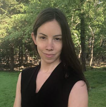 A woman with long dark hair, wearing a black sleeveless top, stands outdoors in a wooded, grassy area. Her facial expression appears subtly skeptical or knowing—fitting for commentary on Bitcoin policy debates—and no text or identifying information is visible in the image.