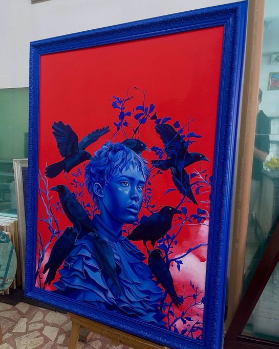 A striking painting with a thick blue frame depicts a blue-toned figure surrounded by black birds against a vivid red background.