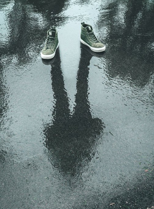 Pair of olive green high-top sneakers placed on a wet reflective puddle, with their reflection creating a mirrored image.