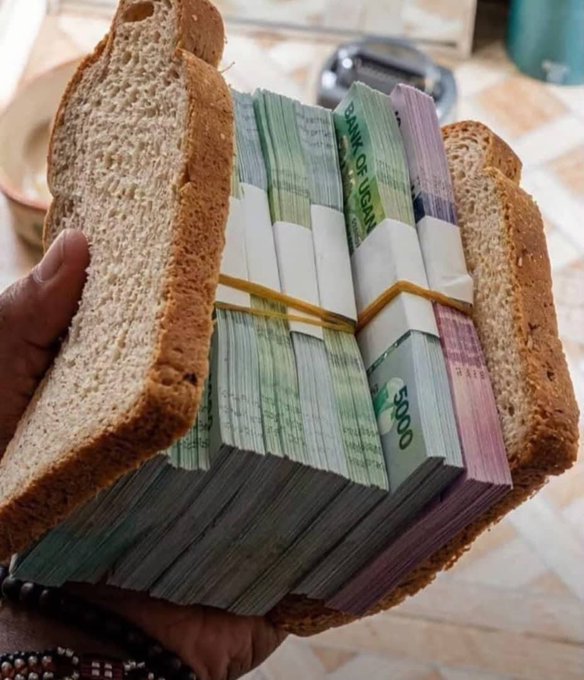 A hand holds an open sandwich-like object made of bread slices containing thick stacks of banknotes (Thai currency) bound with rubber bands.