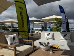 An outdoor lounge area with umbrellas, seating, and Robinhood branded flags and banners under a cloudy sky.