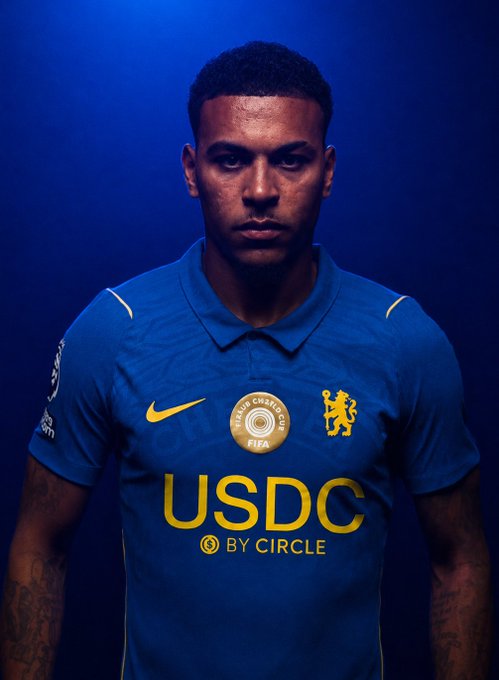 A young man models the new Chelsea FC kit against a blue backdrop, with "USDC BY CIRCLE" displayed prominently in yellow on the front of the shirt, alongside the Chelsea lion crest and a circular FIFA Club Champions badge. The image showcases Circle's new main sponsorship deal with the Premier League club.