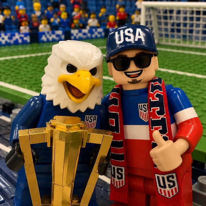 A Lego eagle mascot and a Lego fan wearing a "USA" cap and scarf pose with a golden trophy in a soccer stadium, with visible "US" shield emblems on their outfits, tying into a "gm x" good morning message celebrating American soccer pride.