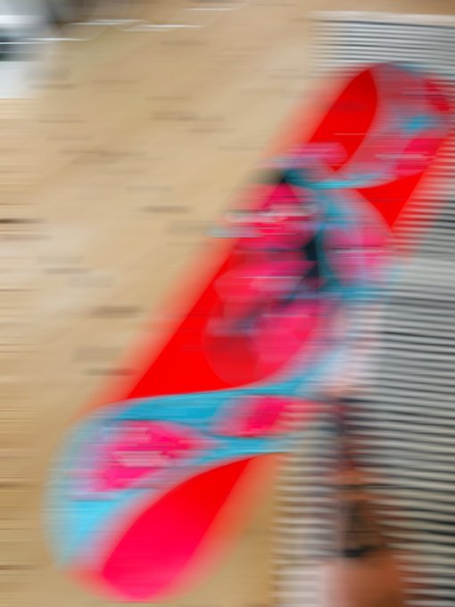 A heavily motion-blurred close-up shows an unclear red, pink, and turquoise object or graphic against a beige indoor background.