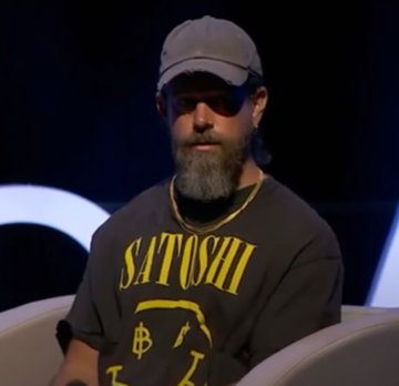 A bearded man wearing a cap and a t-shirt reading "SATOSHI" with a Bitcoin-style "B" symbol sits on a panel, aligning with the post about Jack Dorsey's non-profit expanding support for open source AI and Bitcoin development. The Satoshi-themed attire reflects the post's reference to bitcoin as the economic layer for AI agent transactions.