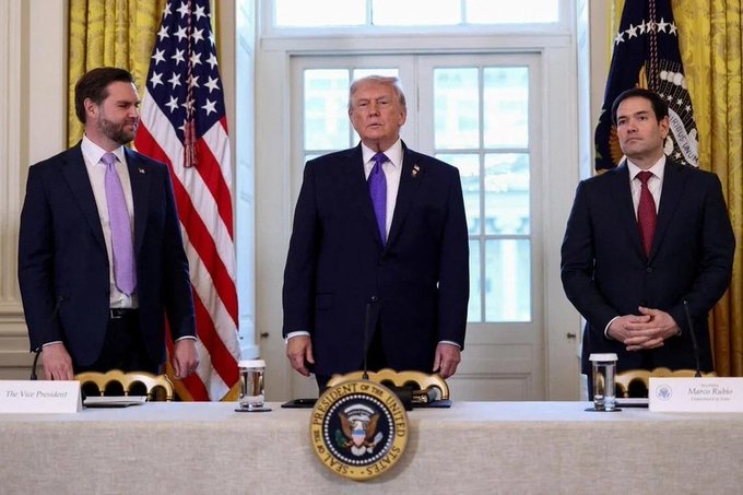 Three men in suits stand behind a podium bearing the Presidential Seal at the White House, with nameplates for 'The Vice President', 'Donald Trump', and 'Marco Rubio' visible in front of American flags.