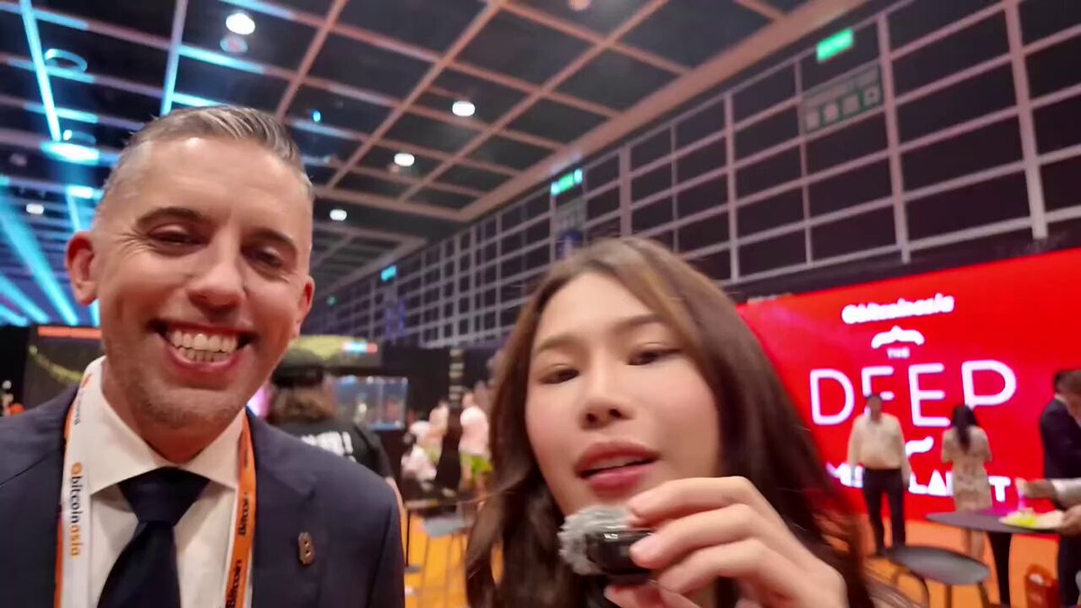 "At #Bitcoin Asia last August, Matt Cole said Strive planned to buy over $700M worth of Bitcoin Fast forward: Strive now holds 16,500 BTC worth over $1.27B and just announced a 4.2B raise to stack even more They are now the 7th largest public Bitcoin holder on the". In this image, there is a man with a woman who has her mouth full of food and she is holding an object that appears to be a cigarette or lighter near some blue lights at the event they are attending. The image also features people in other areas of the room, suggesting it could be a gathering or event with various attendees enjoying themselves.