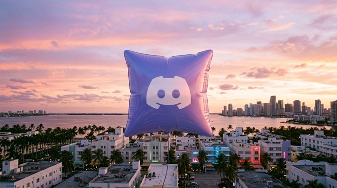 A large purple inflatable balloon displaying the Discord logo floats above a coastal city skyline at sunset, visually promoting the launch of the TouchGrass Discord channel as announced in the accompanying text.