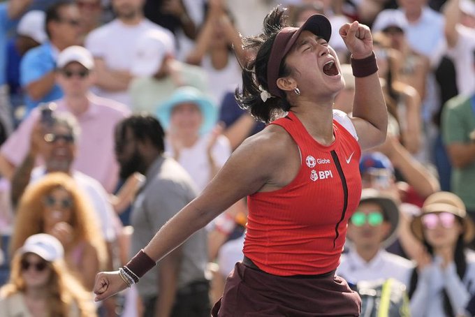 A female tennis player wearing a red Nike top with "Globe" and "BPI" sponsor logos and a maroon visor celebrates triumphantly with a clenched fist raised and mouth open in a victorious shout. The image captures the elation tied to a promotional giveaway post celebrating her potential victory at the US Open.