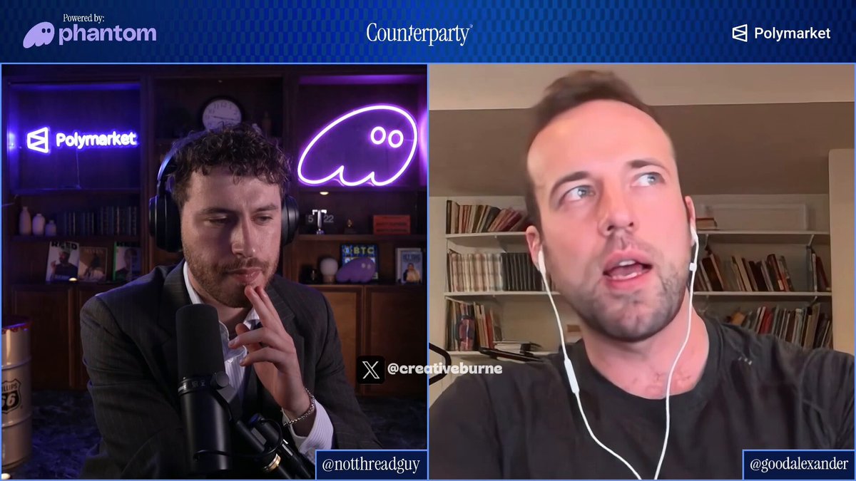 The image shows two men sitting behind microphones, engaged in a conversation or interview. One man appears to be speaking into his microphone while the other man listens attentively with headphones on. The background features a bookshelf filled with various books, suggesting that they might be discussing a topic related to literature or research.