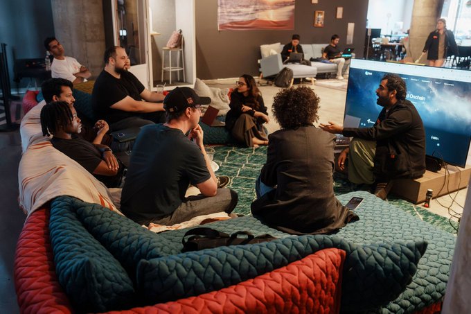 A group of hackers gathers around a TV displaying the "El Dorado" game screen at Runtime in NYC, previewing a new Publish skill while their submissions are stored on Filecoin.