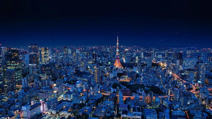 A nighttime aerial view of Tokyo's skyline, prominently featuring the illuminated Tokyo Tower surrounded by the glowing cityscape.