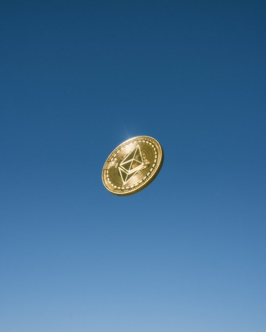 A gold Ethereum cryptocurrency coin floating against a clear blue sky.