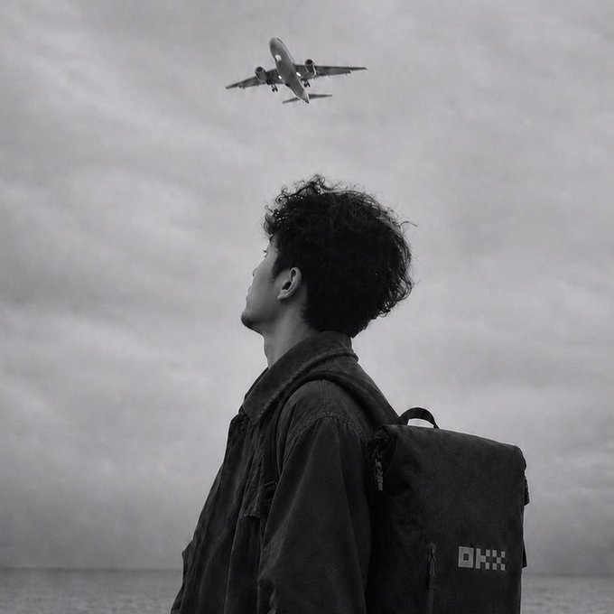A black and white photograph of a young man with curly hair wearing a backpack, looking up at an airplane flying overhead against a cloudy sky.