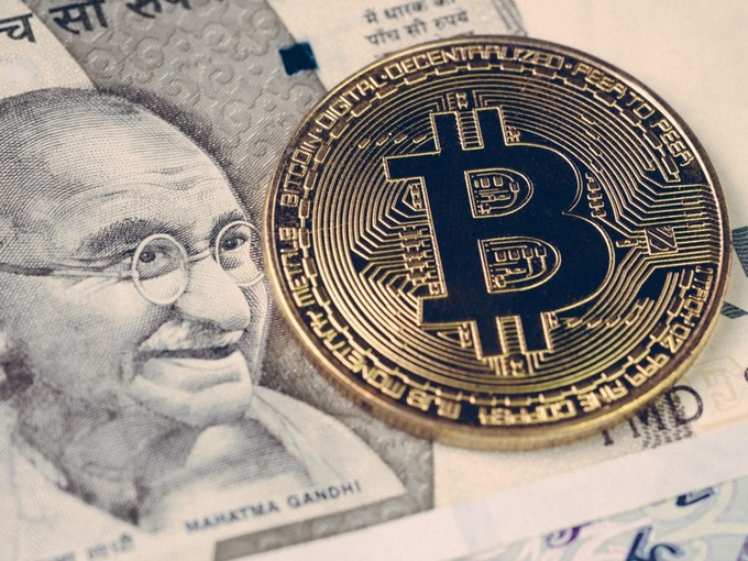 A gold Bitcoin coin rests on top of Indian rupee banknotes featuring Mahatma Gandhi.