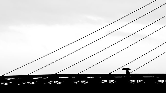 The image features a person walking across an overpass, with their silhouette visible against the backdrop of the bridge. The photo appears to be taken during the day under cloudy skies, creating a moody atmosphere. The caption "Good Morning Happy #TezosTuesday Last 2 pieces Umbrella Man" suggests that this is a post about the person's journey or experience while walking across the overpass.