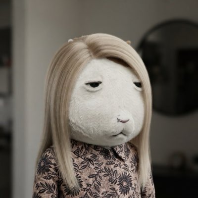A figurine of a person with long blonde hair wearing a floral dress, displaying a deadpan, unimpressed expression with droopy eyes and a slight frown.