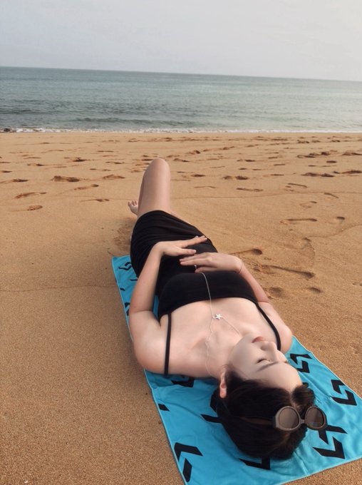 The image features a woman laying down on a beach, wearing a black dress and sunglasses. She appears relaxed and enjoying her time at the beach. The photo also includes text that reads "去年開始和一些朋友在 Bitget 買美股代幣 並由懶麻煩的事情變簡單 也用了一段時間之後", which suggests that the photo may have been taken during a special event or occasion. The woman's attire and the beach setting create an atmosphere of leisure, relaxation, and enjoyment.