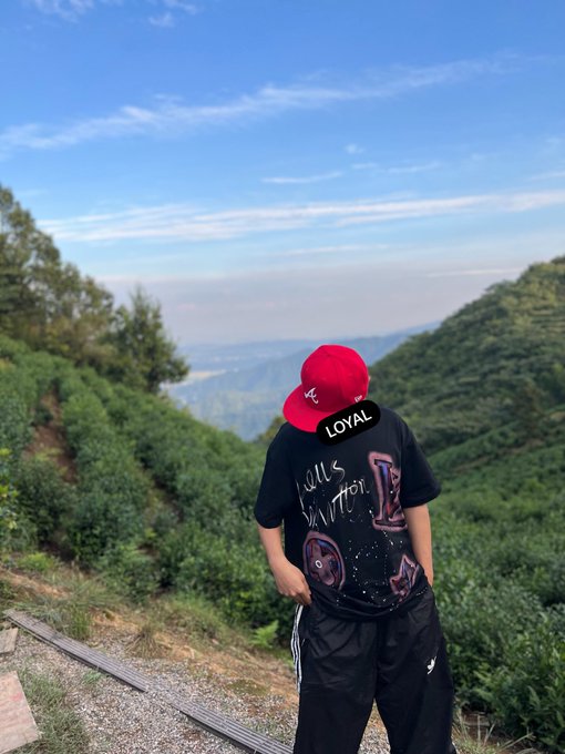 A person wearing a red cap and a black shirt with "LOYAL" sticker and "Let is better" text stands overlooking a scenic mountain valley, reflecting on the pursuit of wealth and repayment.

The image's expansive landscape symbolizes the long journey of seeking wealth to repay debt, with the figure gazing into the distance as if contemplating the road ahead.