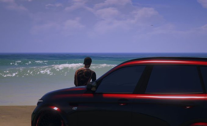 A person with a heart tattoo on their back stands on a beach beside a black SUV with glowing red trim, looking out at the ocean under a blue sky.
