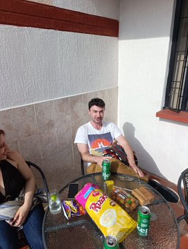 The image shows a man sitting at an outdoor table with various food items, including chips, soda cans, and a bag of chips. The man appears to be enjoying his time outdoors while eating some snacks. There are also two other people present in the scene, one on each side of the main subject. A cell phone is visible near the bottom left corner of the image.

The post that has been mentioned is related to the monero barbeque and seems to be a social media account or a news outlet sharing information about it. The man sitting at the table with food items appears to be engaged in conversation, while the other two people are also present but not directly involved in the main subject's activities.