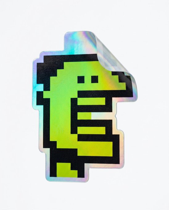 A holographic sticker featuring a pixelated green character with a black outline, shown with its backing paper partially peeled away.