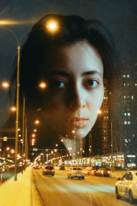A double exposure portrait merges a young woman's contemplative face with a nighttime urban street scene, where glowing streetlights, illuminated skyscrapers, and traffic blend seamlessly with her features. Her direct gaze and neutral expression evoke a sense of quiet introspection that complements the bustling yet lonely cityscape woven into her image. No visible text or numbers appear in the composition. The accompanying post "Very cool;" aptly captures the artistic and visually striking nature of this surreal, dreamlike photograph.
