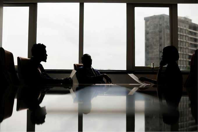 Silhouetted figures sit around a conference table in front of floor-to-ceiling windows, with a city skyline visible in the background, evoking the executive meetings and corporate discussions that define industry gatherings like Sibos. The image pairs with commentary from finance leaders, including Bank of America and Finastra executives, on the future of real-time treasury and 24/7 payments.