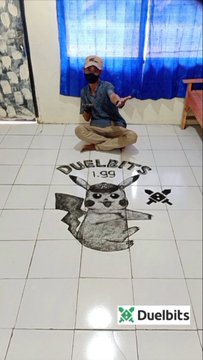 A man kneels on a tiled floor beside a large floor graphic featuring a cartoon dog, crossed weapons, and the text “DUELBITS 1.00,” with a Duelbits logo at the bottom. The post praises the creative display and says that if @DuelbitsJasper tips him $1,000 to distribute to the community, he would tip the creator $150.