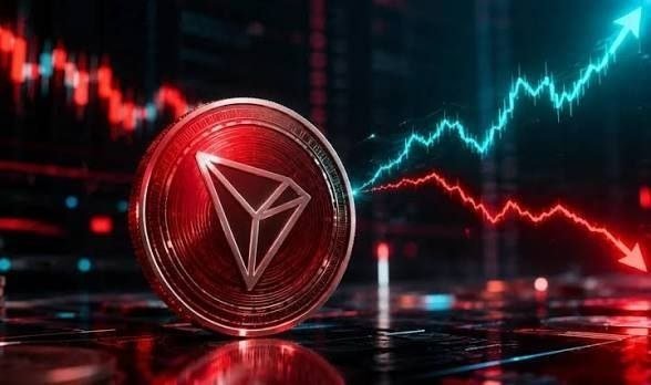 A 3D rendering of a red Tron (TRX) cryptocurrency coin in the foreground, with a trading chart showing rising green and falling red lines in the background.