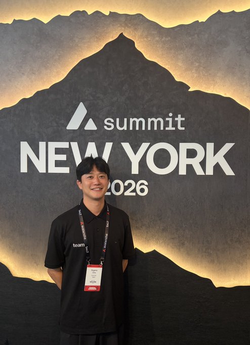 A man wearing an Algorand 'team' lanyard and badge poses smiling in front of a backdrop reading 'Summit NEW YORK 2026' with a mountain silhouette.