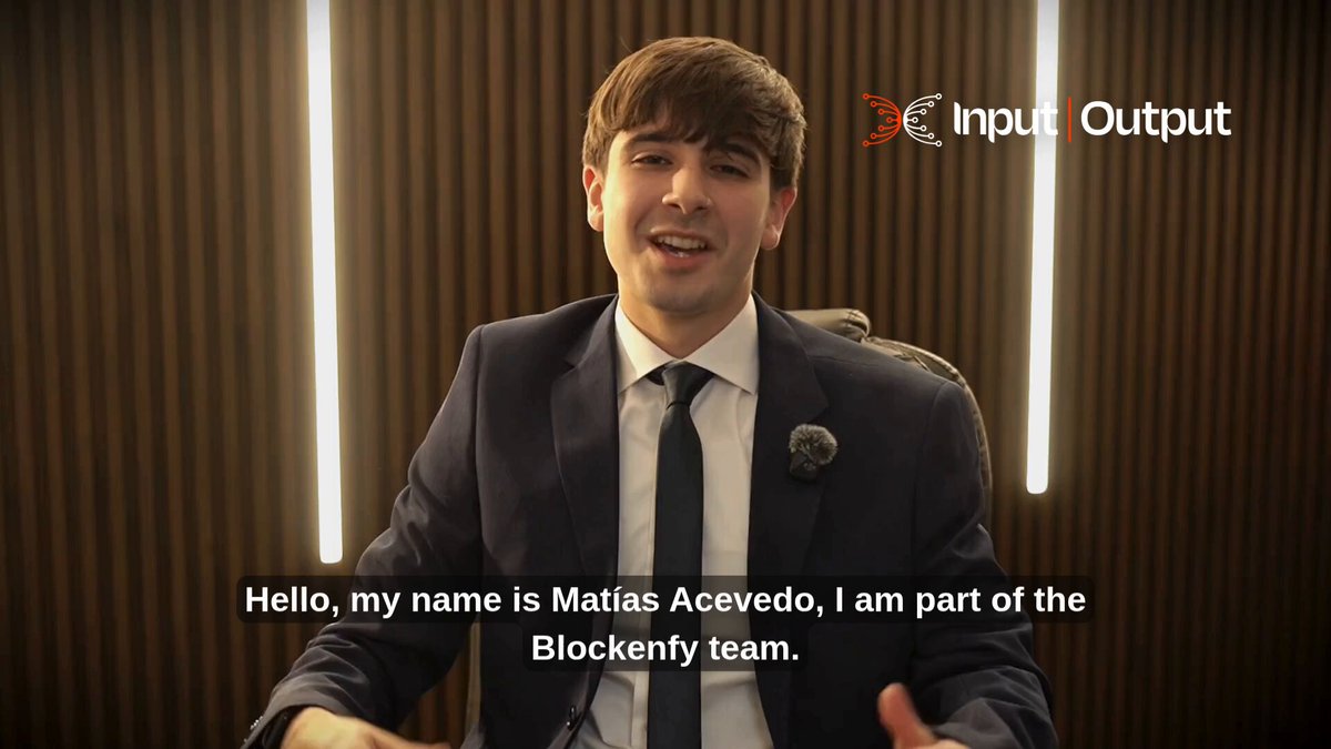 The image features a man dressed in a suit and tie sitting behind a desk with his arms outstretched as if he's giving a speech or presentation. The background of the image shows a brown wall, which contrasts with the white text on the image that reads "Hello, my name is Matias Acvedo, I am part of the Blockneyy team."