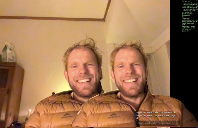 A man smiles broadly in what appears to be a duplicated or mirrored selfie, with a code overlay on the right side and chat text at the bottom referencing 'duplicate the person'.