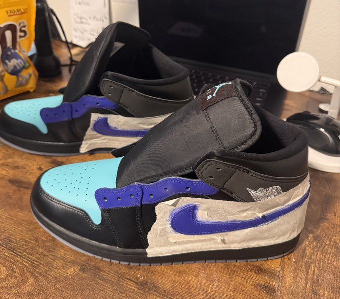 Custom Air Jordan 1 mid sneakers with a black, light blue, and purple color scheme, featuring masking tape detail on the side panels.