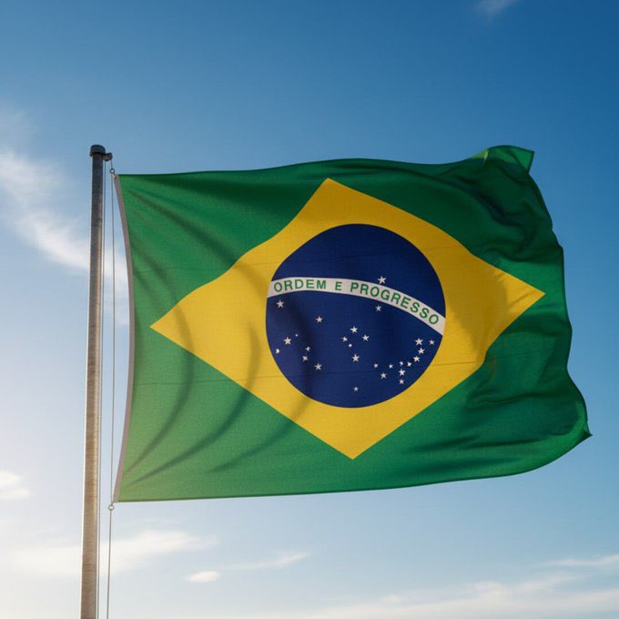 The flag of Brazil with 'ORDEM E PROGRESSO' on the celestial globe, waving against a blue sky.