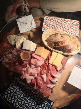 Overhead view of a table spread with an assortment of cured meats, cheeses, and bread, accompanied by a glass of red wine and decorative napkins.