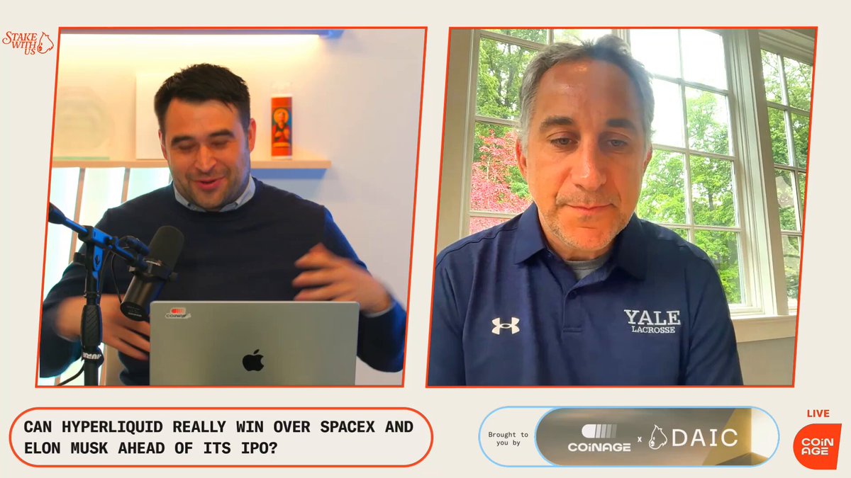 The image shows two men sitting at a desk with an Apple laptop, engaged in a conversation on a webinar or video call. One man is actively speaking into the microphone while the other listens attentively. The room also features a window overlooking the outdoors. The focus of the photo is on this interaction between the two individuals and their discussion regarding the recent $SPCX IPO.