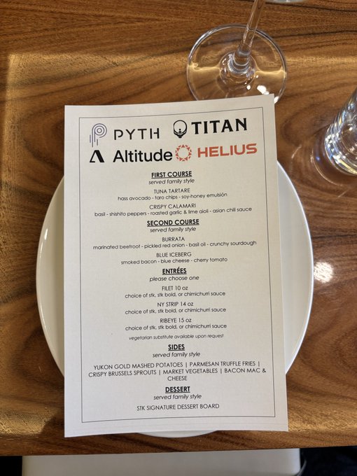 A menu photographed on a wooden table featuring logos for Pyth, Titan, Altitude, and Helius, with courses like Tuna Tartare, Burrata, Blue Iceberg, and filet mignon.