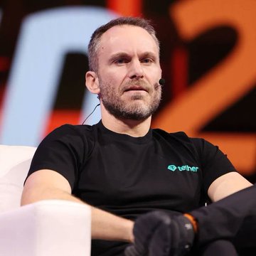 A man with a short beard, wearing a black "Tether" branded t-shirt and a headset microphone, is seated on a stage during a conference presentation. The setting and attire align with the accompanying post identifying him as Tether CEO Paolo Ardoino, sharing his views on Bitcoin's longevity.
