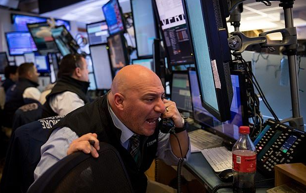 A stock trader on the trading floor talking on a telephone while surrounded by multiple monitors displaying financial data, with a Coca-Cola bottle visible nearby.