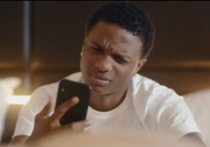 The image shows an adult male wearing a white t-shirt who appears to be looking at his cell phone intently with raised eyebrows or a frowning expression. The man's gaze appears to be focused on something on his phone, possibly reading news or browsing messages. While I cannot see the specific content displayed on the screen, it is clear that the image captures the individual's attention and involvement with their smartphone.