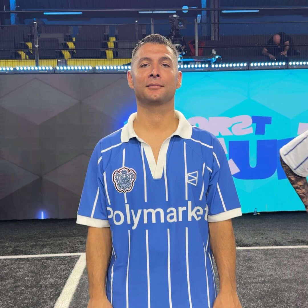 The image features a man wearing a blue and white striped shirt with the word "Polymarker" printed on it. He appears to be posing for a photo, possibly at an event or gathering related to cryptocurrency. The background of the image shows a sports field, suggesting that this could be a sports-related event or a casual gathering where people are enjoying various activities together.

The post about Cryptocurrency is written in white text and includes a reference to Bitcoin, which is often associated with Polymarker. This connection might suggest that the man's shirt represents the company Polymarker, which could be a sponsor of an event or a product related to cryptocurrency.