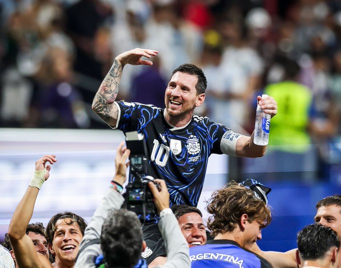 Lionel Messi wearing the number 10 Argentina jersey celebrates with teammates and a water bottle during a soccer match.