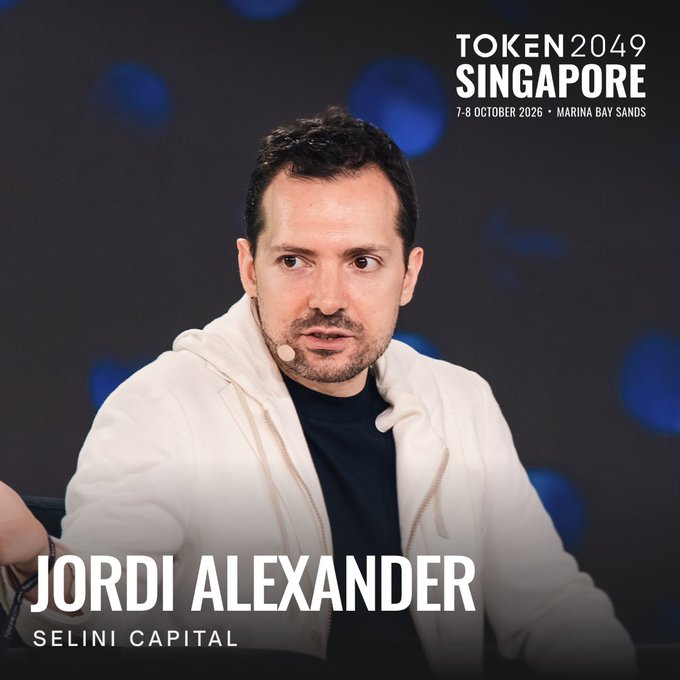 The promotional image for TOKEN2049 Singapore (7-8 October 2026, Marina Bay Sands) features Jordi Alexander, founder of Selini Capital, in a white hoodie against a blurred blue-lit backdrop, with his name and firm displayed prominently at the bottom. The graphic aligns with the post's announcement of his return to the conference, where he will share market insights rooted in his game theory and poker background.