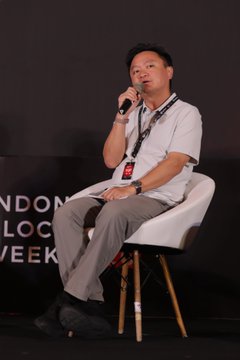 OSL's CCO Eugene Cheung speaks into a microphone while seated on a stage during a panel discussion at Indonesia Blockchain Week, with partial text "NDOM BLOC WEEK" visible in the background.