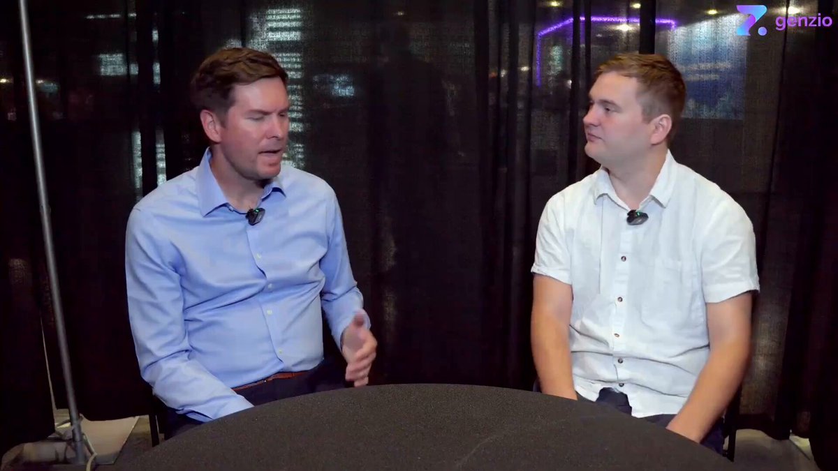 The image shows two men sitting at a table, engaged in a conversation. The background features a black curtain that partially covers their faces, creating an intimate atmosphere for their discussion. The text "More than half of the Fortune 500 is already exploring onchain infrastructure." suggests that this could be related to the emerging trend of companies investing in blockchain technology and cryptocurrencies. The post also mentions that @kylejenke On why enterprises are choosing Optimism to build the next generation of financial products, which implies a connection between the conversation's content and the post's context.