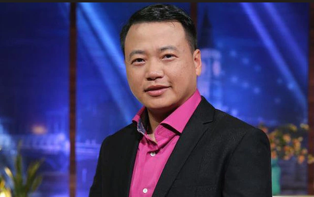 Portrait of an Asian man wearing a black suit jacket over a pink shirt, appearing in a studio setting with a nighttime city backdrop.