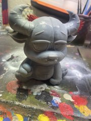 A gray, unpainted 3D-printed figurine of a stylized horned creature sits on a paint-splattered workbench. The handmade sculpt appears to be the type of custom PFP (profile picture) art being promoted in the post about Cavans' hand-painted 3D models.