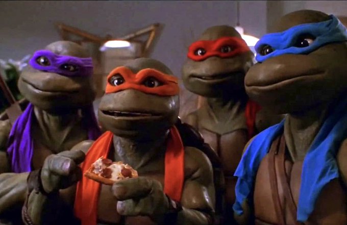 Four costumed characters—the Teenage Mutant Ninja Turtles—stand together, with the orange-masked one (Michelangelo) holding a slice of pizza, their smiling faces bearing a striking resemblance to the Pepe the Frog meme.