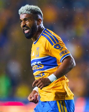 Tigres UANL player with bleached blonde hair and a beard celebrates passionately, wearing the team's iconic yellow and blue striped jersey, in what appears to be a Liga MX match setting. The image relates to the post by showing a Tigres player, likely contributing to the team's 52% probability of defeating Juárez according to Polymarket predictions.